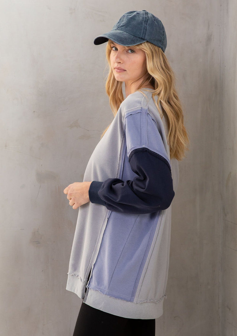 [Color: Grey/Navy] A model wearing a super soft grey and navy blue French terry sweatshirt in a color block paneled design. With a raw edge hemline and a v neckline. An elevated streetwear inspired sweatshirt. 