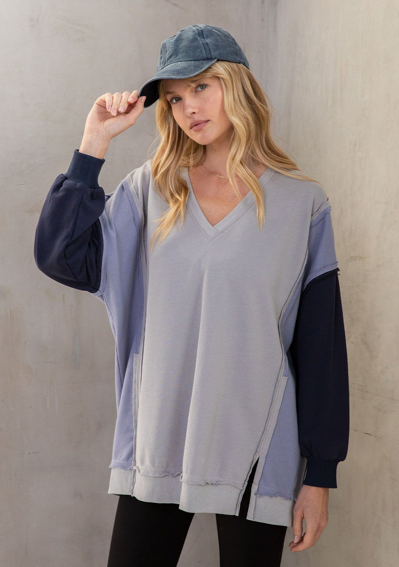 [Color: Grey/Navy] A model wearing a super soft grey and navy blue French terry sweatshirt in a color block paneled design. With a raw edge hemline and a v neckline. An elevated streetwear inspired sweatshirt. 