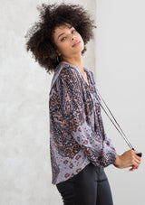 [Color: Grey/Rust] A model wearing a grey and rust paisley print bohemian peasant top. A classic style with long voluminous sleeves, a split v neckline with tassel ties, and a bib yoke detail. 