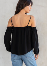 [Color: Black] A model wearing an ultra bohemian billowy black blouse with long attached sleeves, an elastic neckline, and adjustable spaghetti straps. 