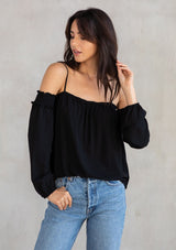 [Color: Black] A model wearing an ultra bohemian billowy black blouse with long attached sleeves, an elastic neckline, and adjustable spaghetti straps. 