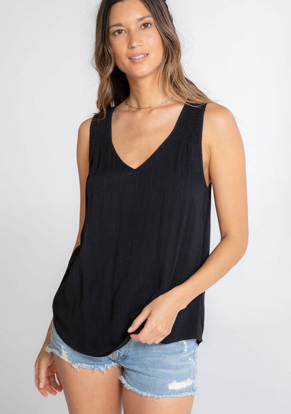 [Color: Black] A model wearing an ultra soft and lightweight black tank top in subtle striped jacquard. With a loose and flowy silhouette, a v neckline, and smocked yoke detail.