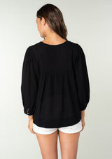 [Color: Black] A back facing image of a brunette model wearing a black cotton bohemian blouse. With long puff sleeves, a flowy relaxed fit, and a lattice front yoke.