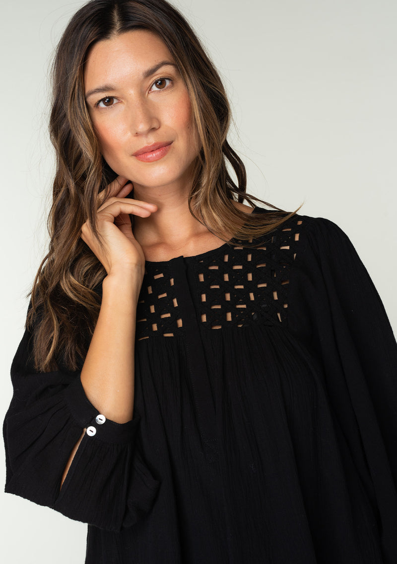 [Color: Black] A close up front facing image of a brunette model wearing a black cotton bohemian blouse. With long puff sleeves, a flowy relaxed fit, and a lattice front yoke.