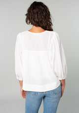 [Color: White] A back facing image of a brunette model wearing a white cotton bohemian blouse. With long puff sleeves, a flowy relaxed fit, and a lattice front yoke. 