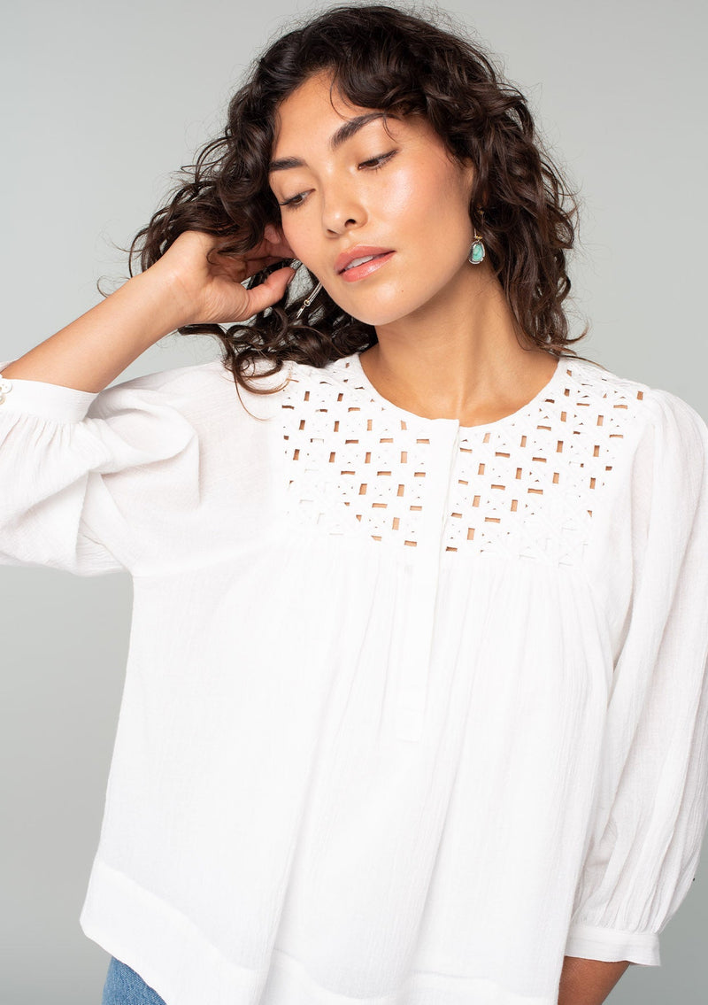 [Color: White] A close up front facing image of a brunette model wearing a white cotton bohemian blouse. With long puff sleeves, a flowy relaxed fit, and a lattice front yoke. 