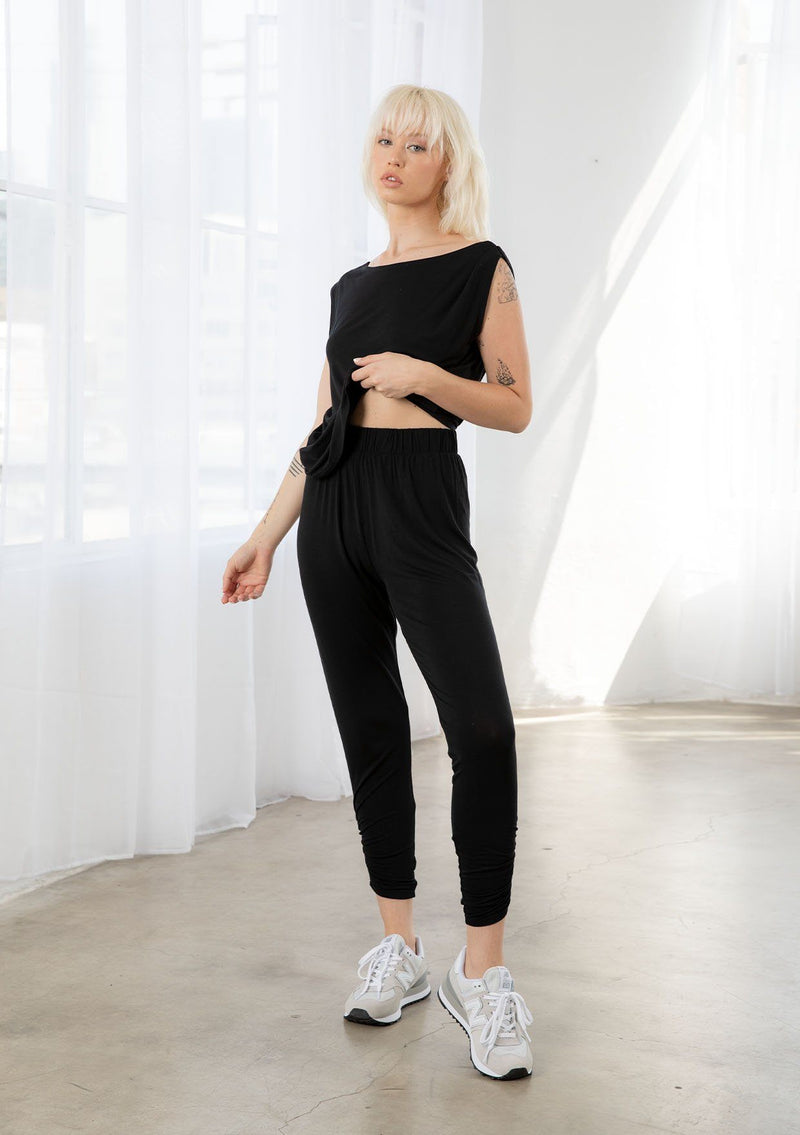 [Color: Black] A model wearing a soft and stretchy legging pant. With a cropped leg, side gathered details at the ankle, and an elastic waist.