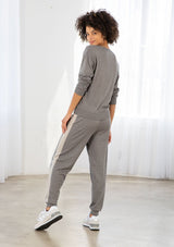 [Color: Heather Smoke/Stone] A model wearing a soft grey jogger pant with a contrast stripe along the side of the leg. Featuring a drawstring waist, a long tapered leg, and ribbed cuff. 