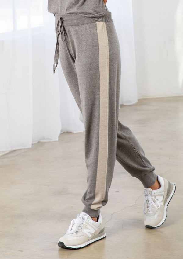 [Color: Heather Smoke/Stone] A model wearing a soft grey jogger pant with a contrast stripe along the side of the leg. Featuring a drawstring waist, a long tapered leg, and ribbed cuff. 