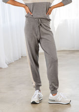 [Color: Heather Smoke/Stone] A model wearing a soft grey jogger pant with a contrast stripe along the side of the leg. Featuring a drawstring waist, a long tapered leg, and ribbed cuff. 