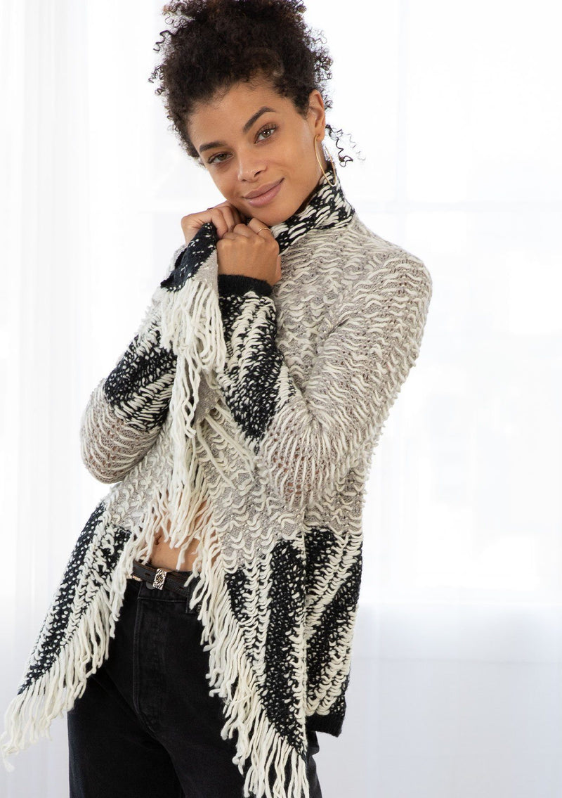 [Color: Light Heather Grey/Black] A model wearing a chunky marled knit bohemian cardigan in a grey and black pattern. With a fringed hemline, long sleeves, and contrast trim.