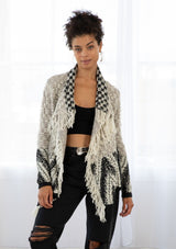 [Color: Light Heather Grey/Black] A model wearing a chunky marled knit bohemian cardigan in a grey and black pattern. With a fringed hemline, long sleeves, and contrast trim.