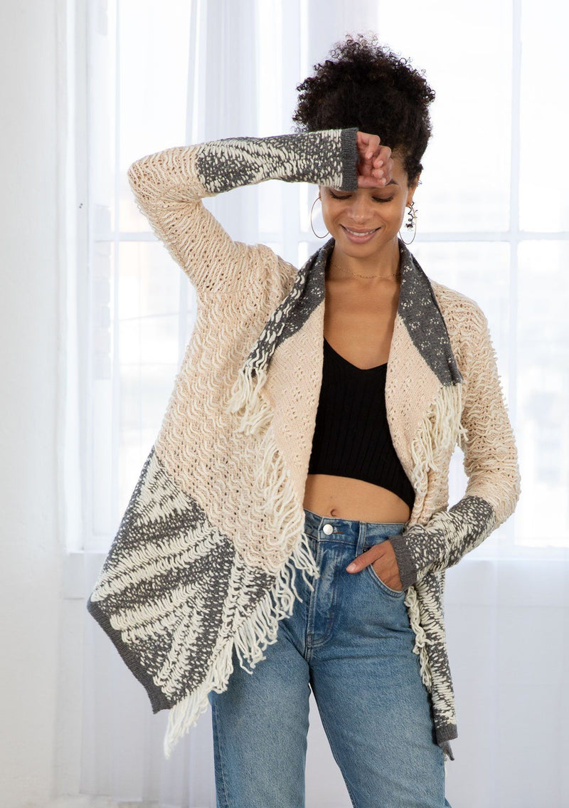 [Color: Heather Nude/Charcoal] A model wearing a chunky marled knit bohemian cardigan in a grey and nude pattern. With a fringed hemline, long sleeves, and contrast trim.