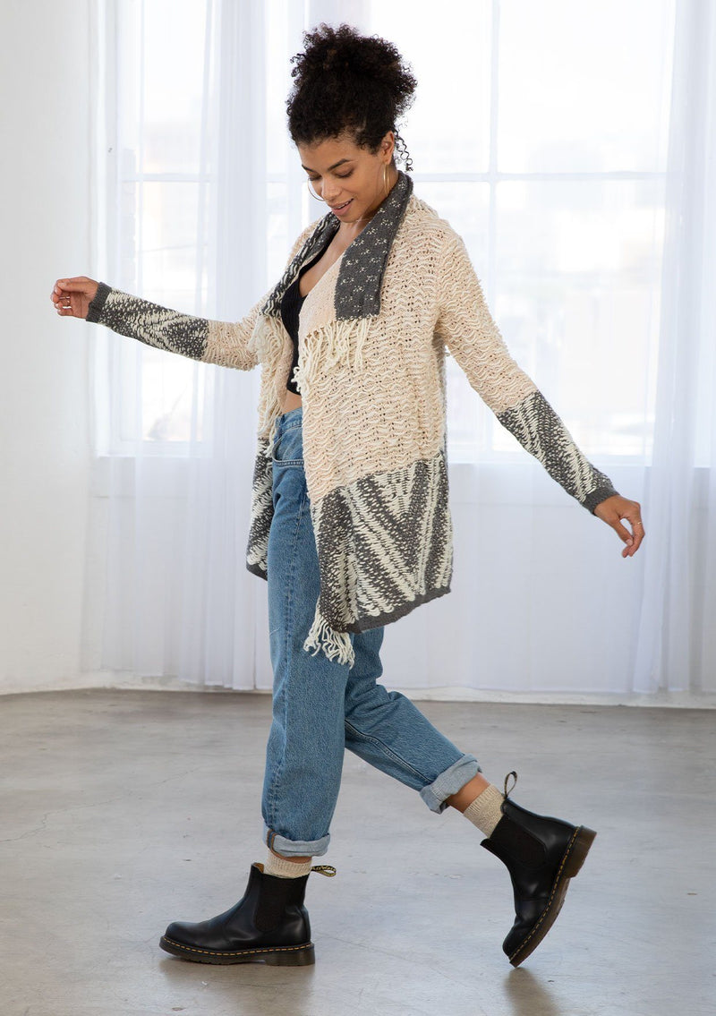 [Color: Heather Nude/Charcoal] A model wearing a chunky marled knit bohemian cardigan in a grey and nude pattern. With a fringed hemline, long sleeves, and contrast trim.