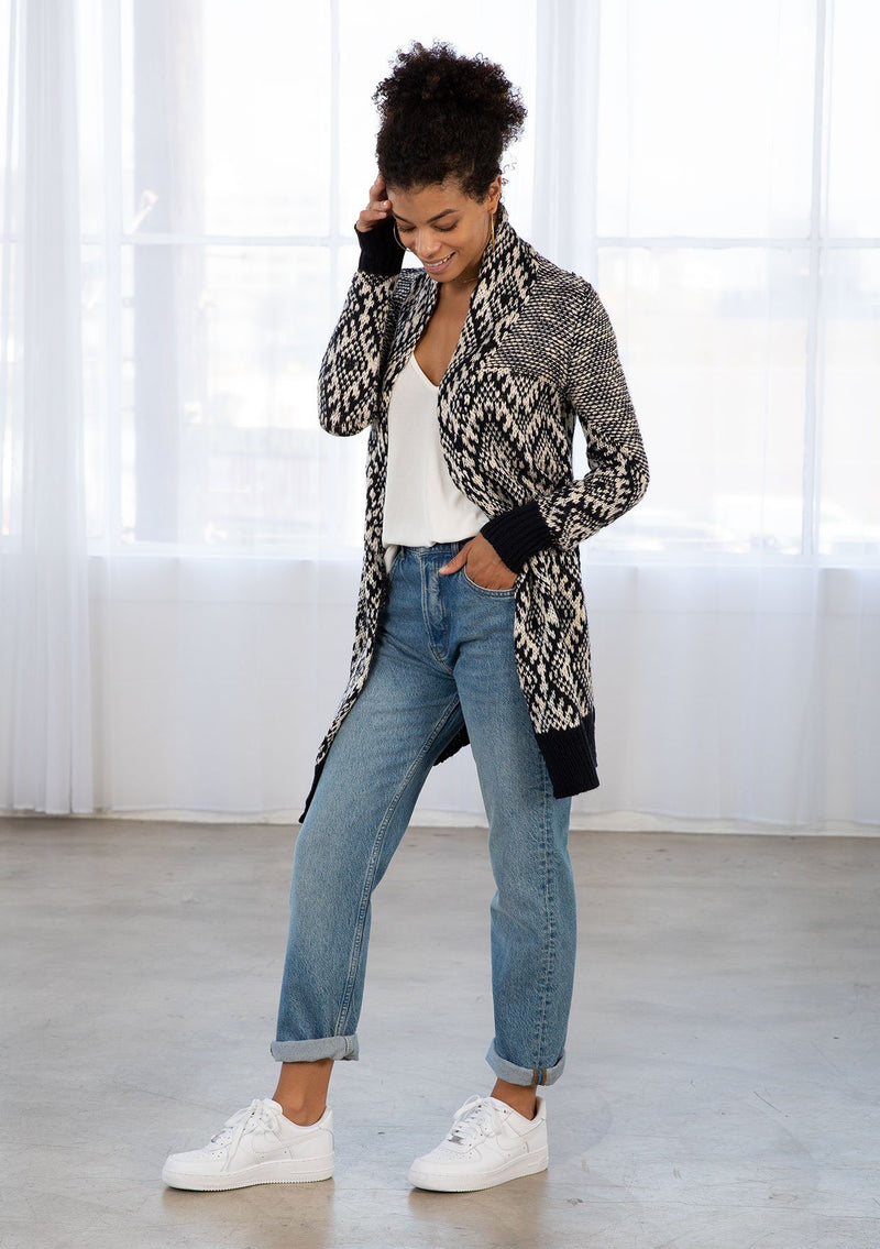 [Color: Navy/Nude] A woman wearing a navy and nude bohemian diamond pattern mid length cardigan. With a shawl collar, an open front, and contrast ribbed trim. 