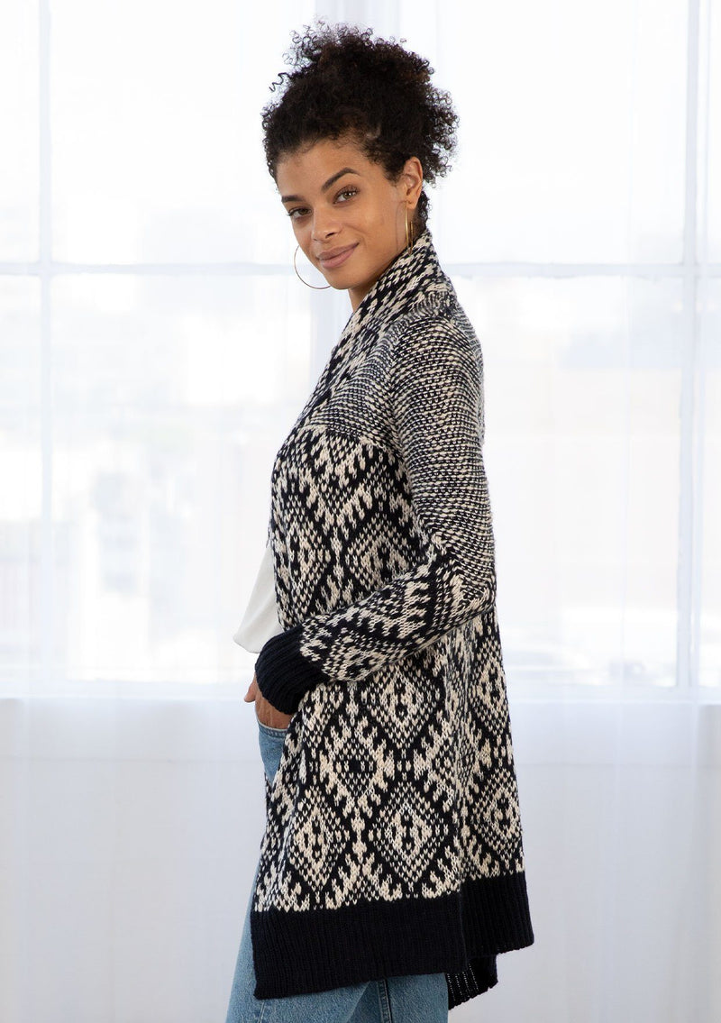 [Color: Navy/Nude] A woman wearing a navy and nude bohemian diamond pattern mid length cardigan. With a shawl collar, an open front, and contrast ribbed trim. 