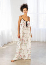 [Color: Cherry/Natural] A model wearing a billowy maxi dress with a carousel print throughout. Featuring a front keyhole detail with tie, side pockets, and spaghetti straps. 