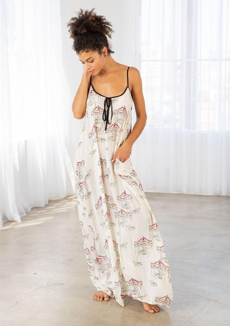 [Color: Cherry/Natural] A model wearing a billowy maxi dress with a carousel print throughout. Featuring a front keyhole detail with tie, side pockets, and spaghetti straps. 