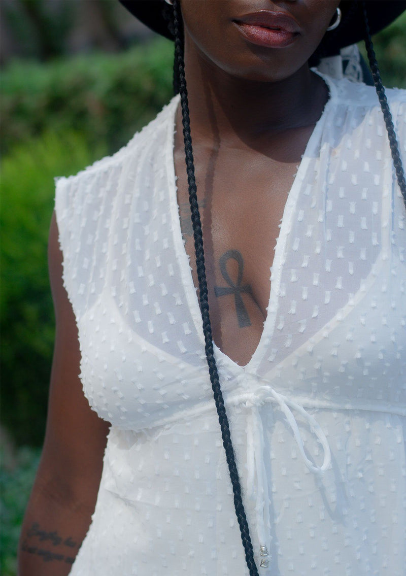 [Color: Off White] A woman wearing a sheer off white chiffon swiss dot maxi dress. With a drawstring empire waist, tiered skirt, v neckline, and lining.