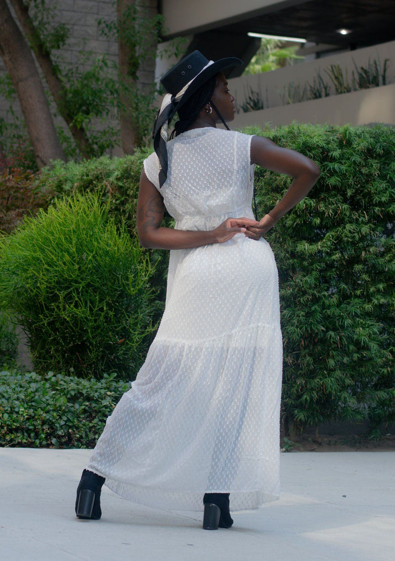 [Color: Off White] A woman wearing a sheer off white chiffon swiss dot maxi dress. With a drawstring empire waist, tiered skirt, v neckline, and lining.