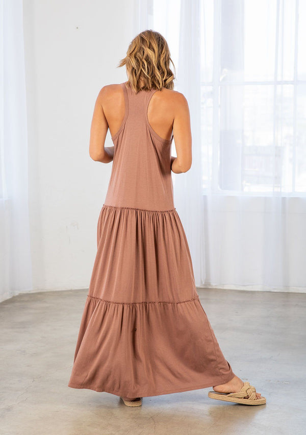 [Color: Clay] A model wearing a timeless cotton blend sleeveless clay brown maxi dress. With a dropped waist, tiered skirt, scooped neckline, and racer back detail.