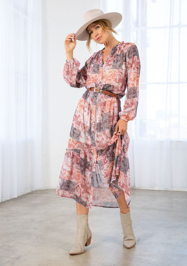 [Color: Natural/Rose] A model wearing a loose and billowy bohemian maxi dress in a red paisley patchwork print. With long voluminous sleeves, a button front, a ruffle trimmed neckline, and a tiered skirt.