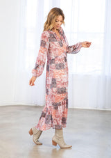 [Color: Natural/Rose] A model wearing a loose and billowy bohemian maxi dress in a red paisley patchwork print. With long voluminous sleeves, a button front, a ruffle trimmed neckline, and a tiered skirt.