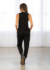 [Color: Black] A model wearing a black soft French terry sleeveless jumpsuit. With a v neckline, side patch pockets, a long tapered leg, and contrast ribbed trim detail. 