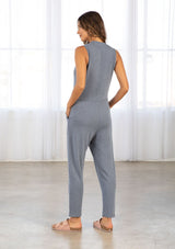 [Color: Denim Blue] A model wearing a blue soft French terry sleeveless jumpsuit. With a v neckline, side patch pockets, a long tapered leg, and contrast ribbed trim detail. 