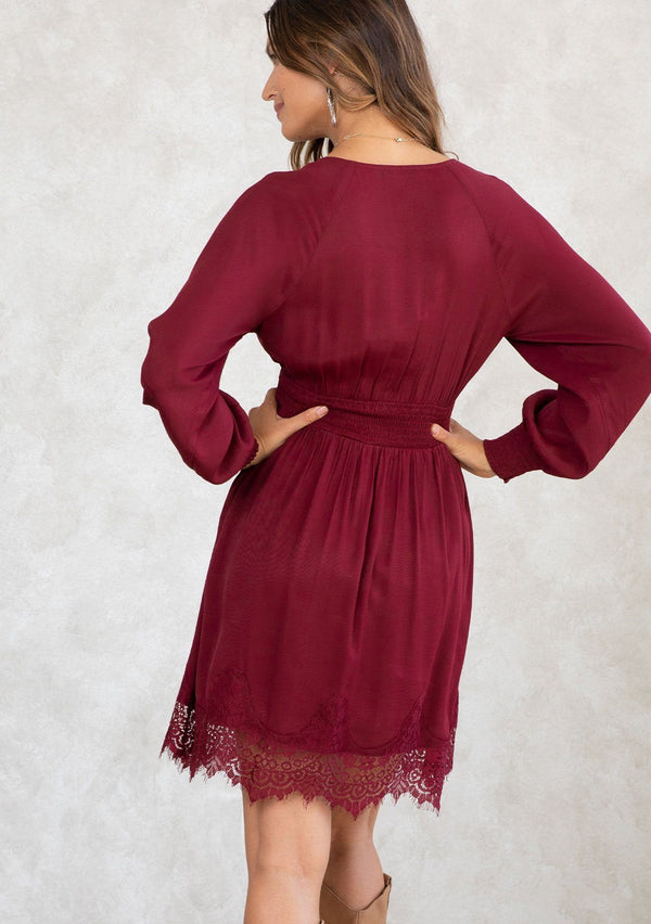 [Color: Merlot] A model wearing a burgundy red mini dress. With long voluminous sleeves, a smocked elastic wrist cuff and waist, and a scalloped lace hemline. A bohemian holiday mini dress. 