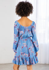 [Color: Azure/Mulberry] A model wearing a timeless bohemian mini dress in a vibrant blue floral print. With long voluminous sleeves and an elastic wrist cuff, a tiered skirt, a front tassel tie, an elastic waist, and a round elastic neckline that can be worn on or off the shoulder. 