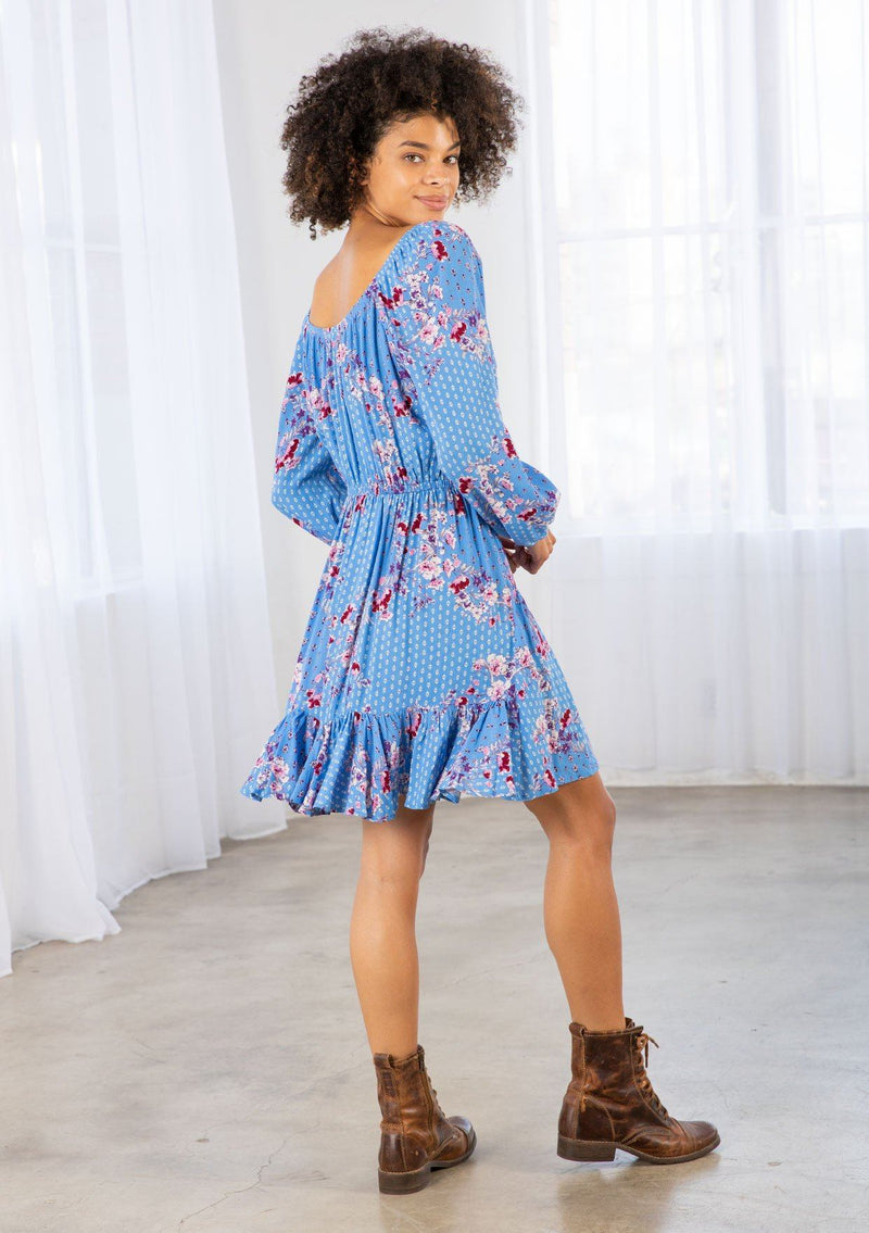 [Color: Azure/Mulberry] A model wearing a timeless bohemian mini dress in a vibrant blue floral print. With long voluminous sleeves and an elastic wrist cuff, a tiered skirt, a front tassel tie, an elastic waist, and a round elastic neckline that can be worn on or off the shoulder. 