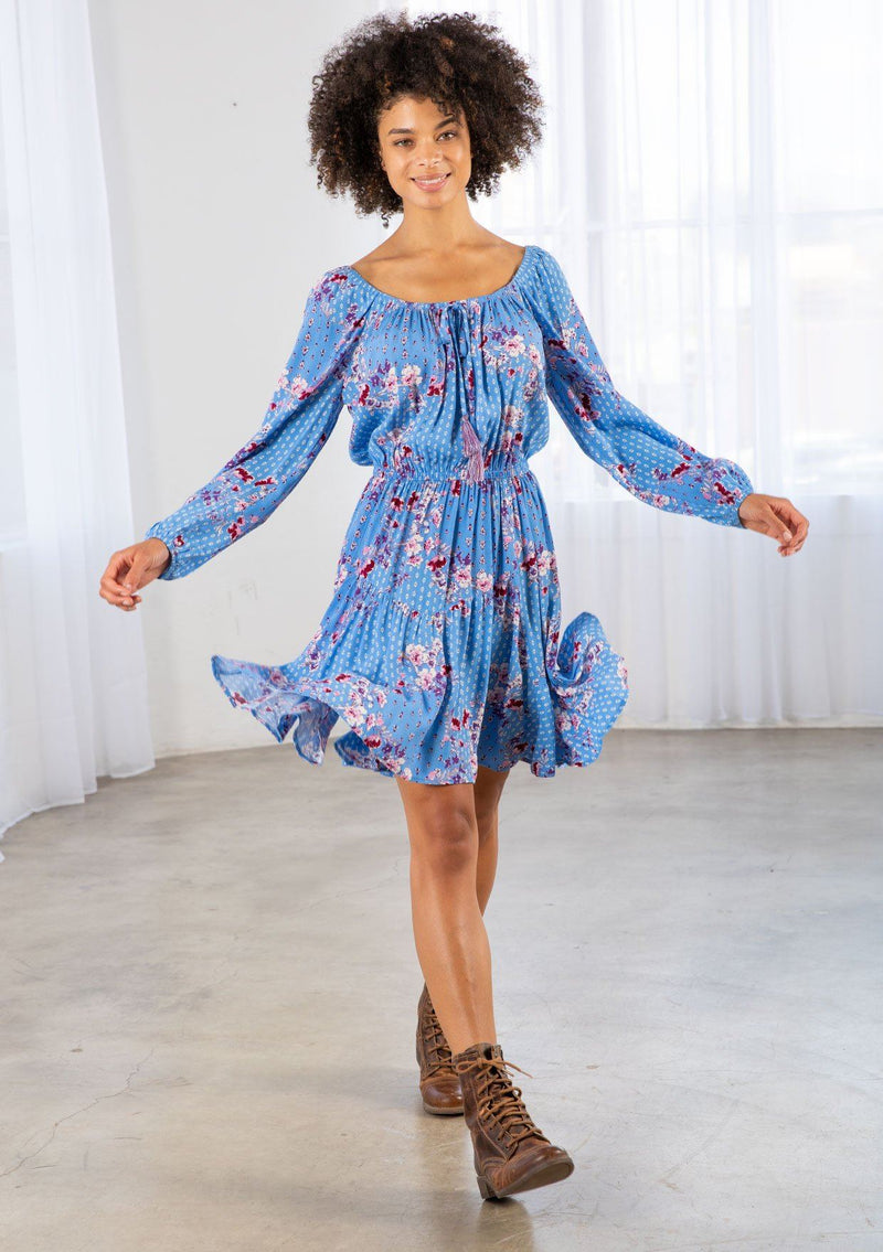 [Color: Azure/Mulberry] A model wearing a timeless bohemian mini dress in a vibrant blue floral print. With long voluminous sleeves and an elastic wrist cuff, a tiered skirt, a front tassel tie, an elastic waist, and a round elastic neckline that can be worn on or off the shoulder. 