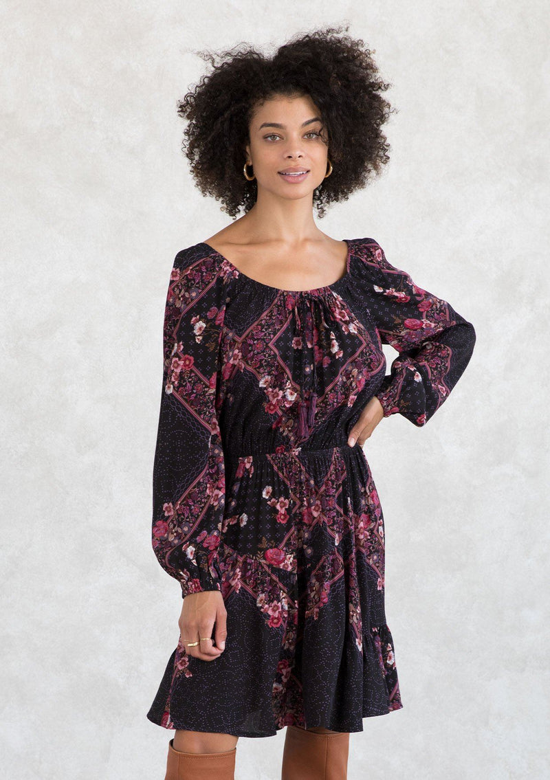 [Color: Plum/Berry] A model wearing a classic bohemian mini dress in an autumnal pink and purple floral print. With an elastic round neckline with tassel tie accent, long voluminous sleeves, and a tiered skirt. 