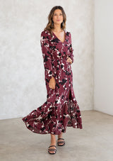 [Color: Merlot/Ivory] A model wearing a merlot red blossom floral print maxi dress. With a mini pom trimmed v neckline, an elastic waist, a side slit, voluminous long sleeves with an elastic wrist cuff, and attached lining. 