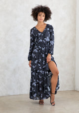 [Color: Slate/Grey] A model wearing a slate blue and grey blossom floral print maxi dress. With a mini pom trimmed v neckline, an elastic waist, a side slit, voluminous long sleeves with an elastic wrist cuff, and attached lining. 