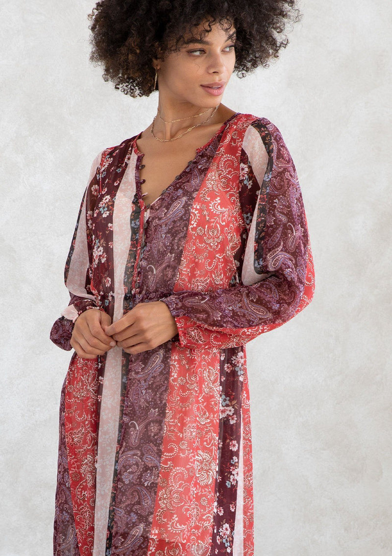 [Color: Brick Red/Plum] A model wearing a sheer red and purple maxi dress in a bohemian floral patchwork print. With long voluminous sleeves, a loop button front, and side slits. 