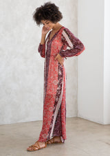 [Color: Brick Red/Plum] A model wearing a sheer red and purple maxi dress in a bohemian floral patchwork print. With long voluminous sleeves, a loop button front, and side slits. 