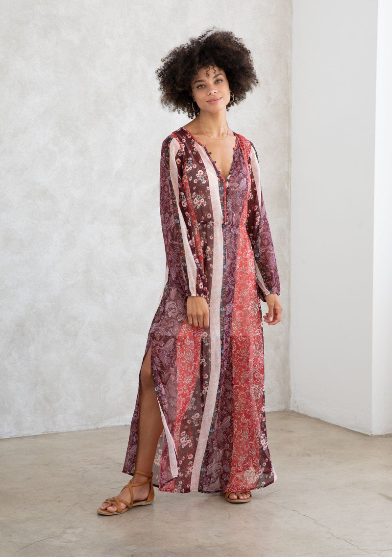 [Color: Brick Red/Plum] A model wearing a sheer red and purple maxi dress in a bohemian floral patchwork print. With long voluminous sleeves, a loop button front, and side slits. 