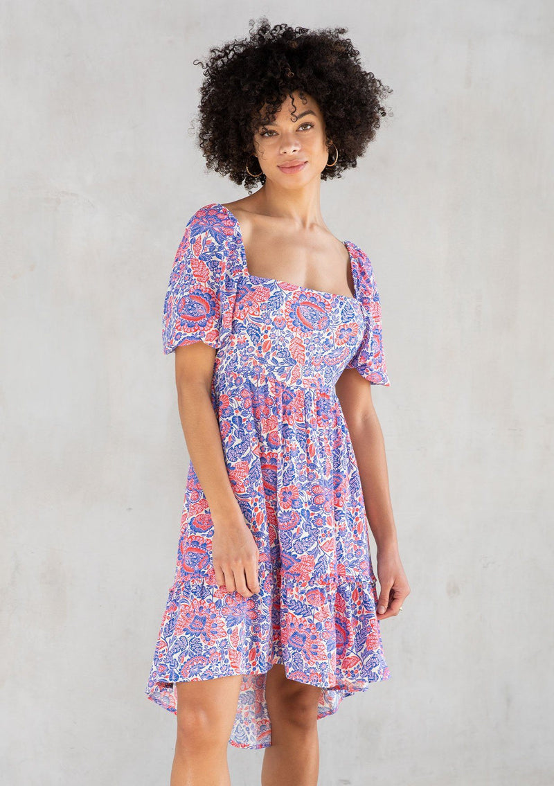 [Color: Ivory/Cobalt] A model wearing a bohemian mini dress in a red and blue paisley print. With short puff sleeves, a square neckline, and an adjustable tassel tie drawstring waist. 