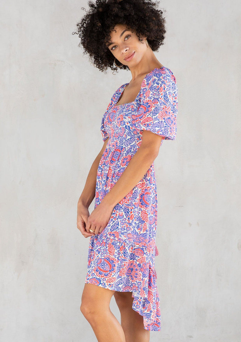 [Color: Ivory/Cobalt] A model wearing a bohemian mini dress in a red and blue paisley print. With short puff sleeves, a square neckline, and an adjustable tassel tie drawstring waist. 