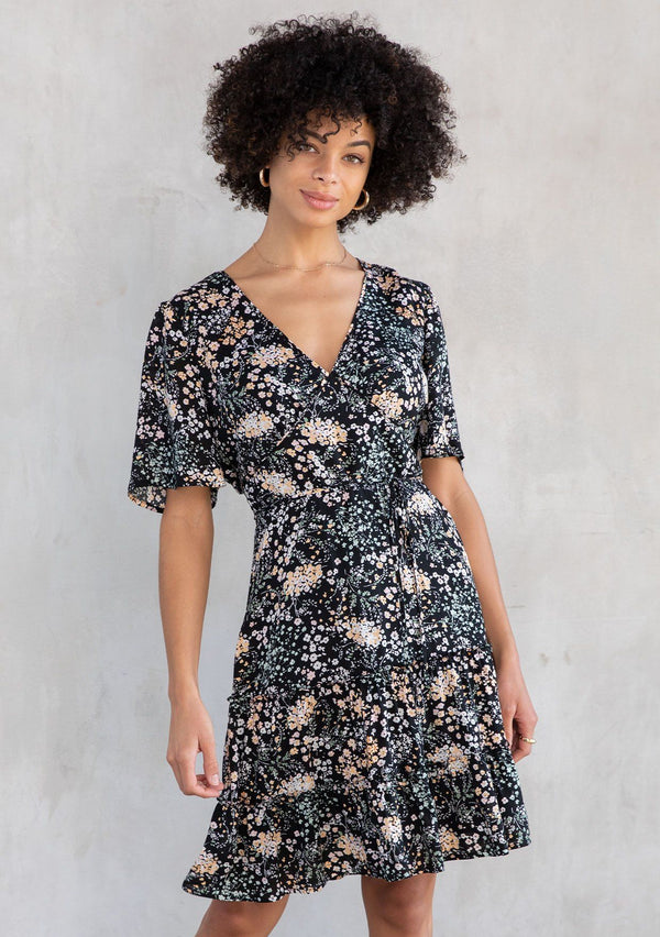 [Color: Black/Mint] A model wearing a trending Spring mini dress in a green floral print. An ultra flattering fit and flare silhouette, with short flutter sleeves and a half elastic waist.