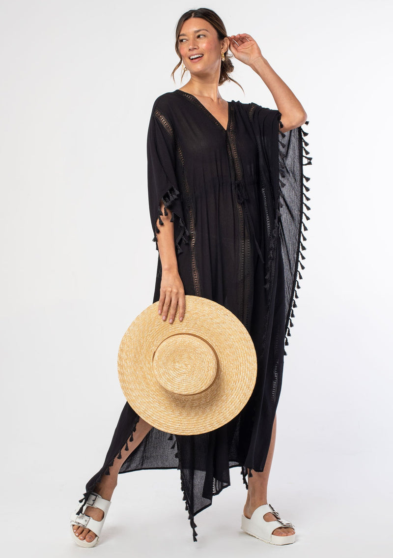 [Color: Black] A woman wearing a sheer black bohemian beach cover up maxi dress with lace and tassel trim and side slits. A kimono kaftan maxi dress perfect for vacations! 