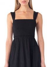 [Color: Black] A close up front facing image of a blonde model wearing a black sleeveless spring mini dress. With wide tank top straps, a square neckline, a smocked slim fit bodice, an empire waist, and a ruffle trimmed tiered skirt.