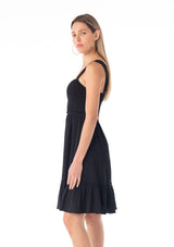 [Color: Black] A side facing image of a blonde model wearing a black sleeveless spring mini dress. With wide tank top straps, a square neckline, a smocked slim fit bodice, an empire waist, and a ruffle trimmed tiered skirt.