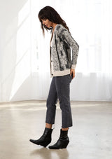 [Color: Black/Cream] A model wearing a cozy black and cream speckled cardigan. With a large button front and a v neckline. 