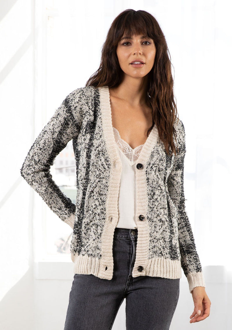 [Color: Black/Cream] A model wearing a cozy black and cream speckled cardigan. With a large button front and a v neckline. 