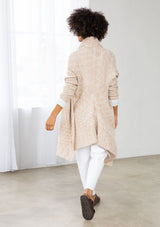 [Color: Nude/Ivory] A model wearing a beige knit reversible cardigan. With long sleeves, a waterfall open front, side pockets, and a shawl collar. 