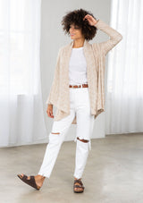 [Color: Nude/Ivory] A model wearing a beige knit reversible cardigan. With long sleeves, a waterfall open front, side pockets, and a shawl collar. 