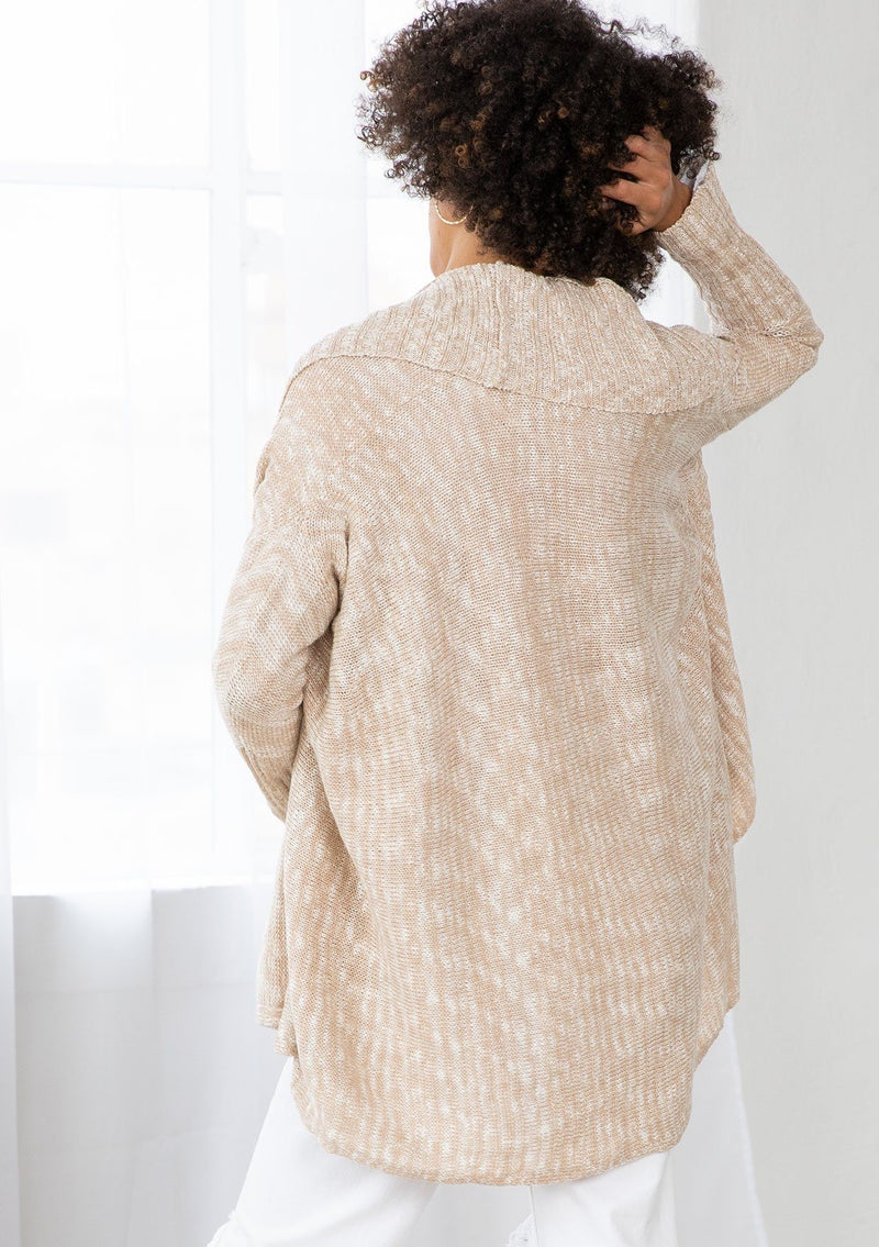 [Color: Nude/Ivory] A model wearing a beige knit reversible cardigan. With long sleeves, a waterfall open front, side pockets, and a shawl collar. 